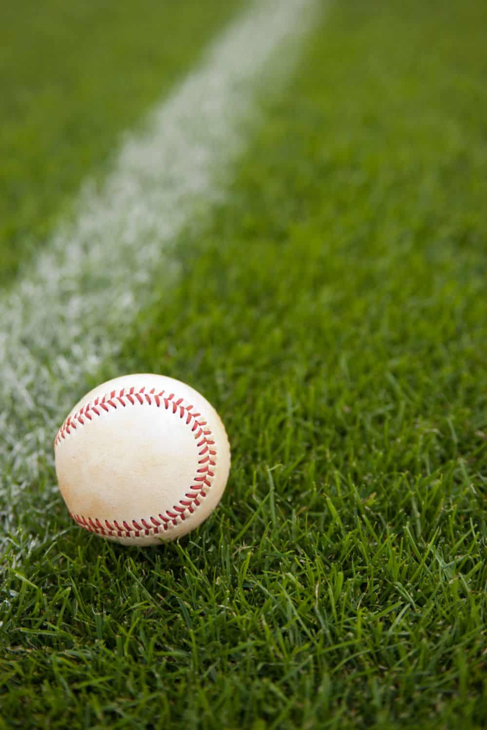 A baseball rests on green grass by a white boundary line, with the focus on the ball and vivid texture of the AZ Turf and Pavers surface clearly visible.