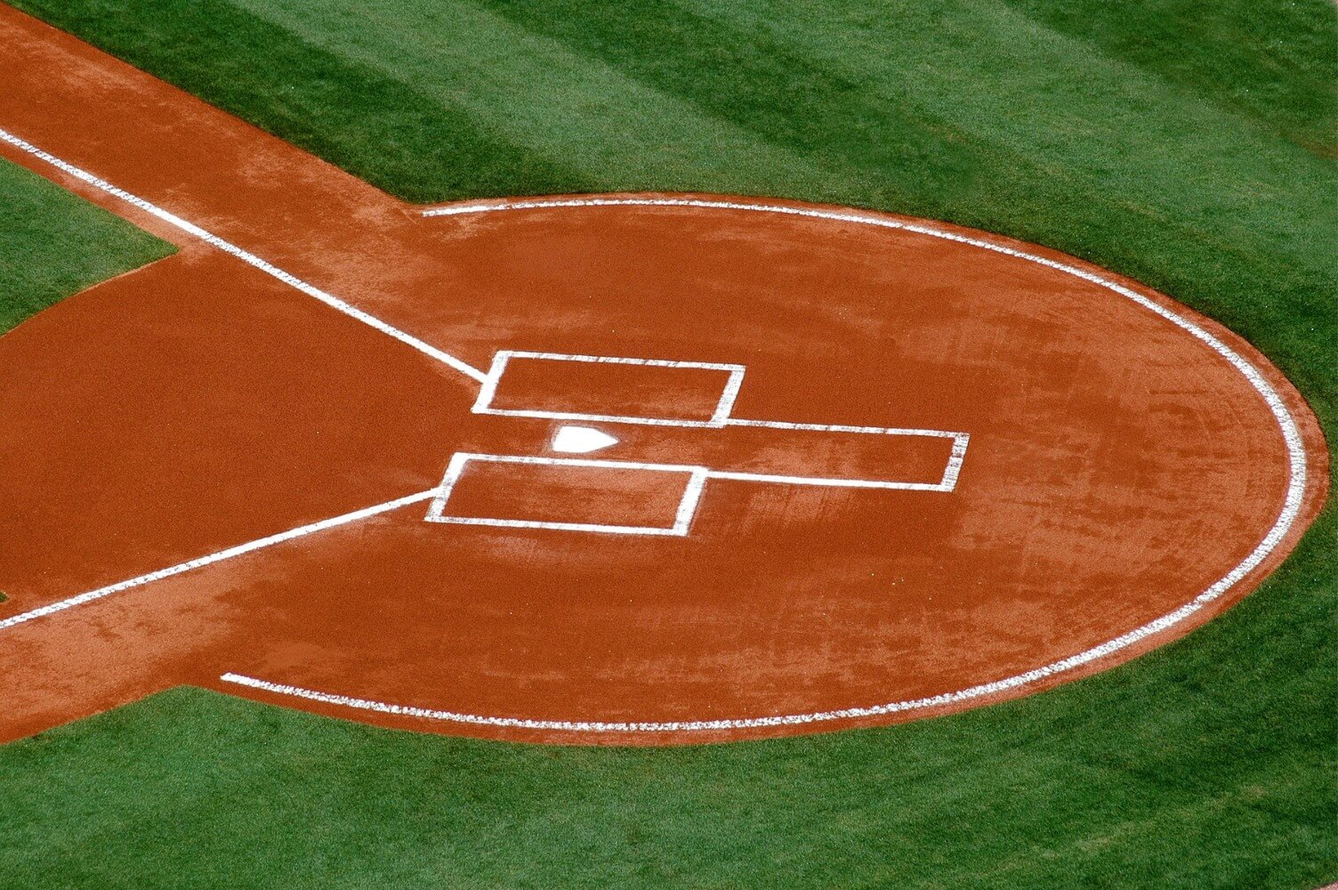 Aerial view of a baseball field's home plate area, featuring freshly painted white lines on reddish-brown dirt and lush green grass, expertly maintained by AZ Turf and Pavers.