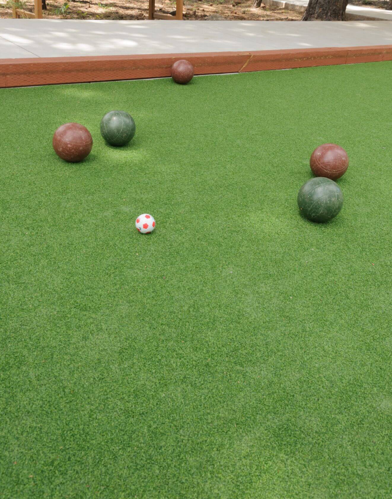 A bocce ball court with four large balls—two green, two brown—and a small white and red target ball on artificial grass by AZ Turf and Pavers. A wooden border outlines the expertly crafted court.